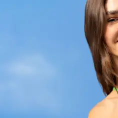 Uśmiechnięta kobieta trzymająca dezodorant Nivea Derma Control na tle błękitnego nieba.